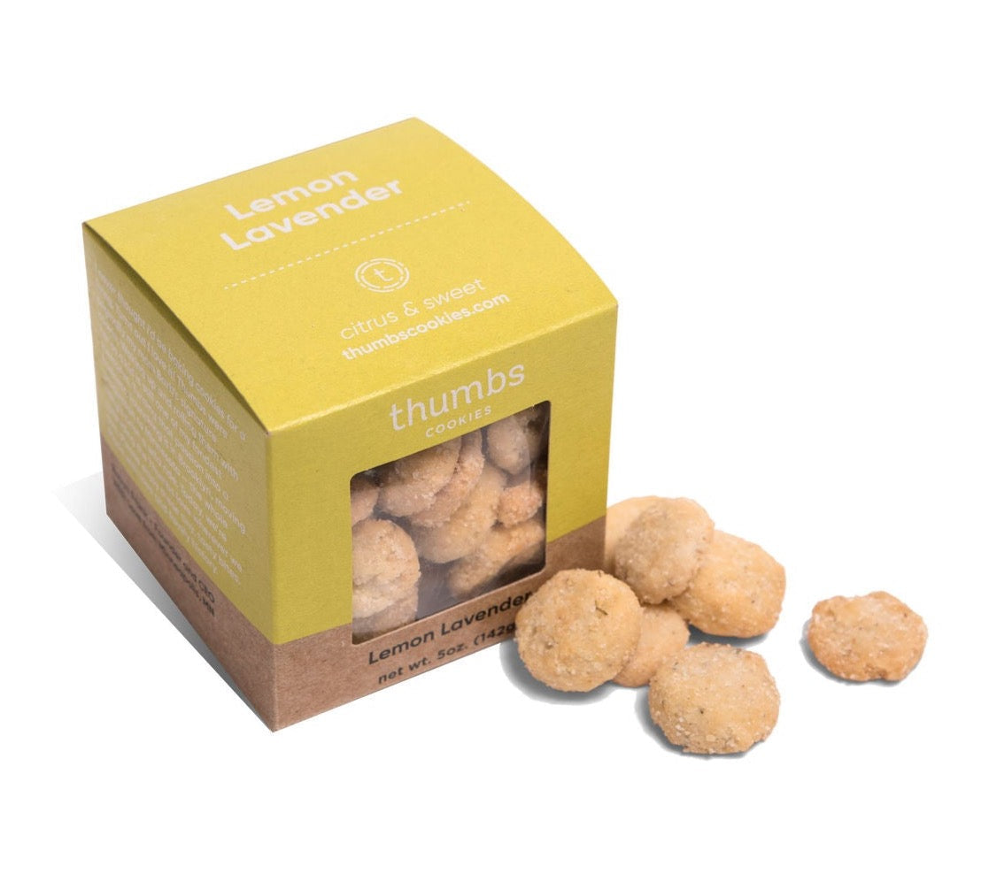 A box labeled "Thumbs Cookies" with lemon lavender flavor is paired with round cookies that have a light, citrusy color and subtle purple specks. The net weight is 5 oz (142g).